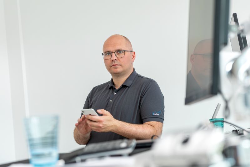 Mann in einem Büro, der ein Smartphone hält und konzentriert in die Kamera schaut.